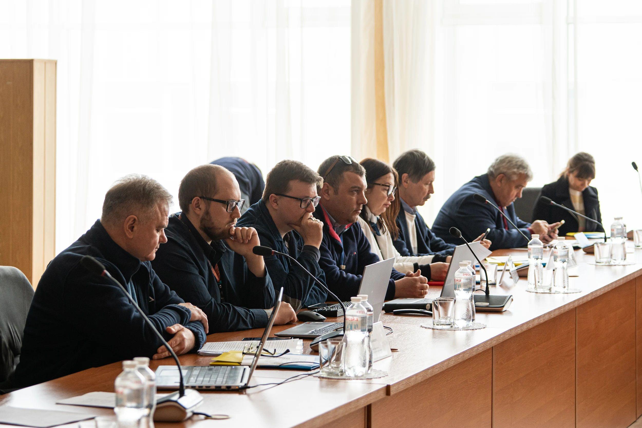 На фото чоловіки сидять за столом під час зустрічі