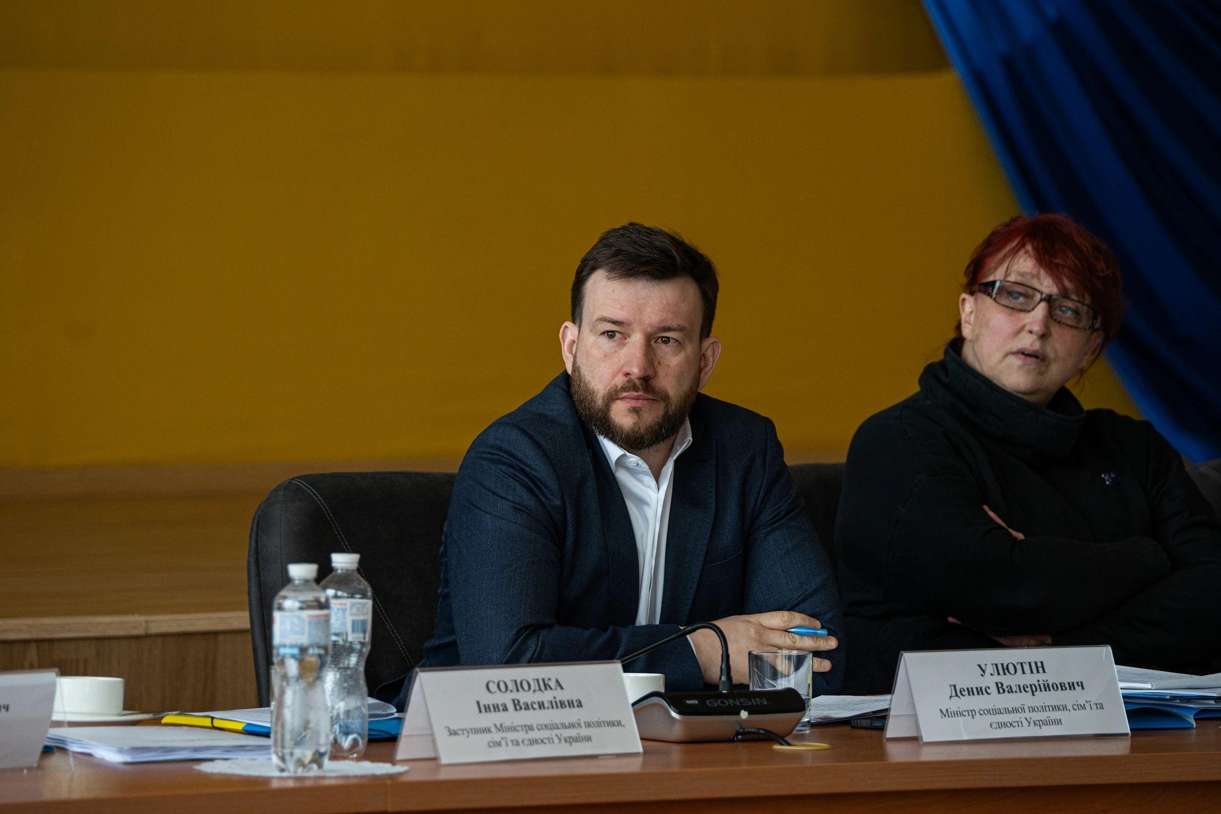 На фото чоловік та жінка сидять за столом під час слухань