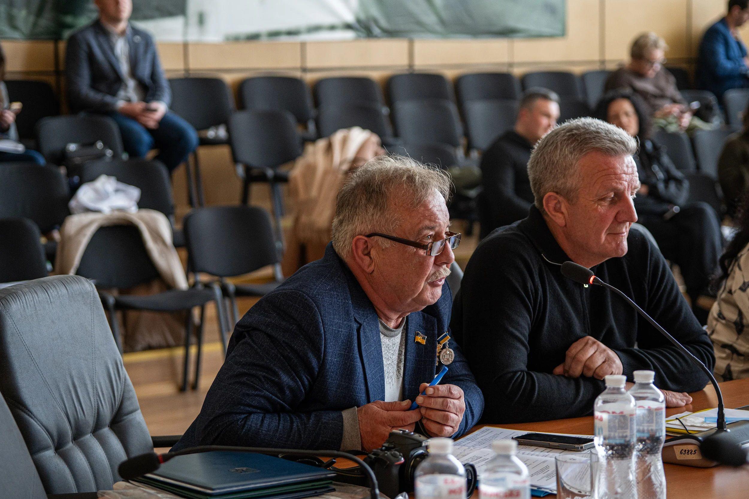 На фото чоловіки сидять за столом під час слухань