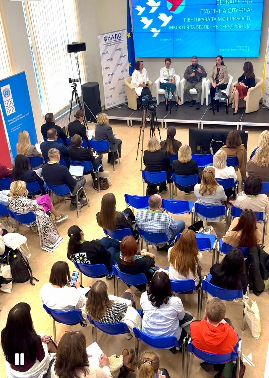На фото жінки та чоловіки сидять у приміщенні під час заходу