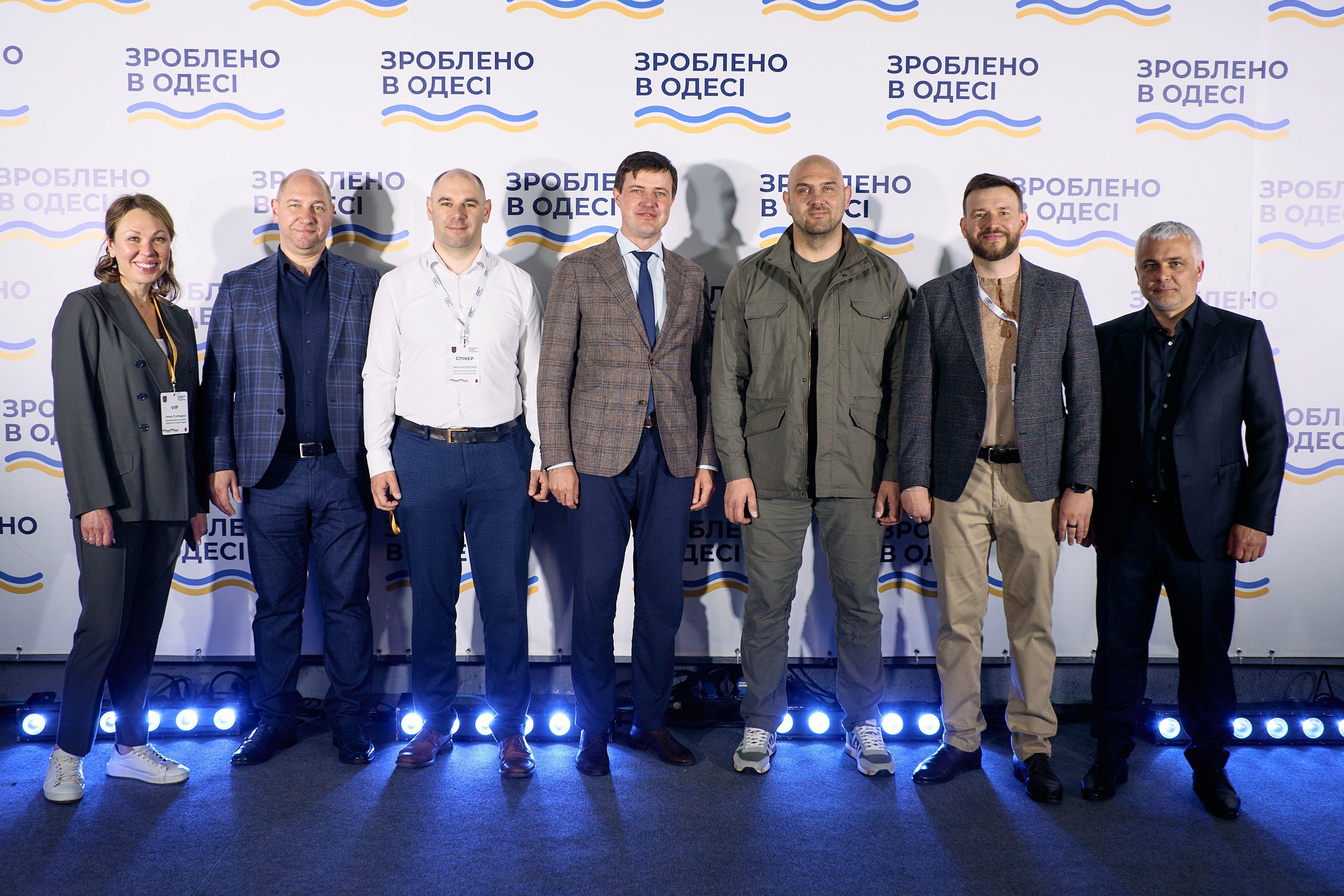 На фото жінка та чоловіки стоять на фоні банеру