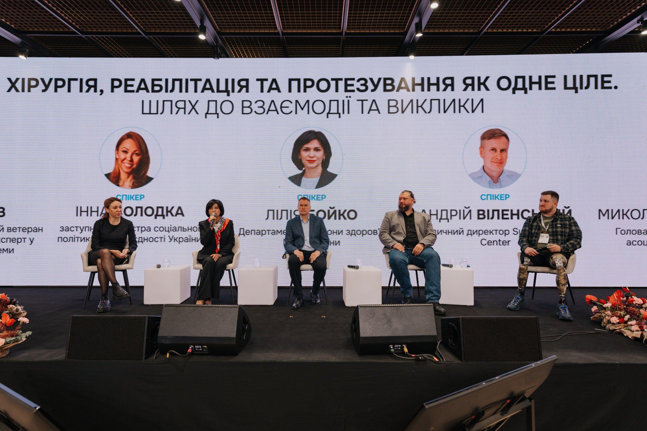 На фото чоловіки та жінки сидять на фоні сцени під час заходу