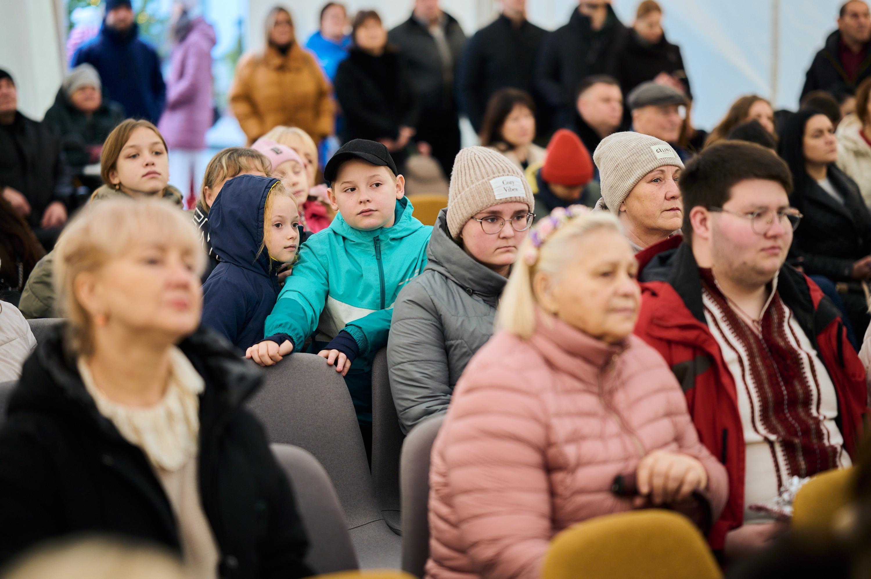 На фото жінки та чоловіки сидять у залі