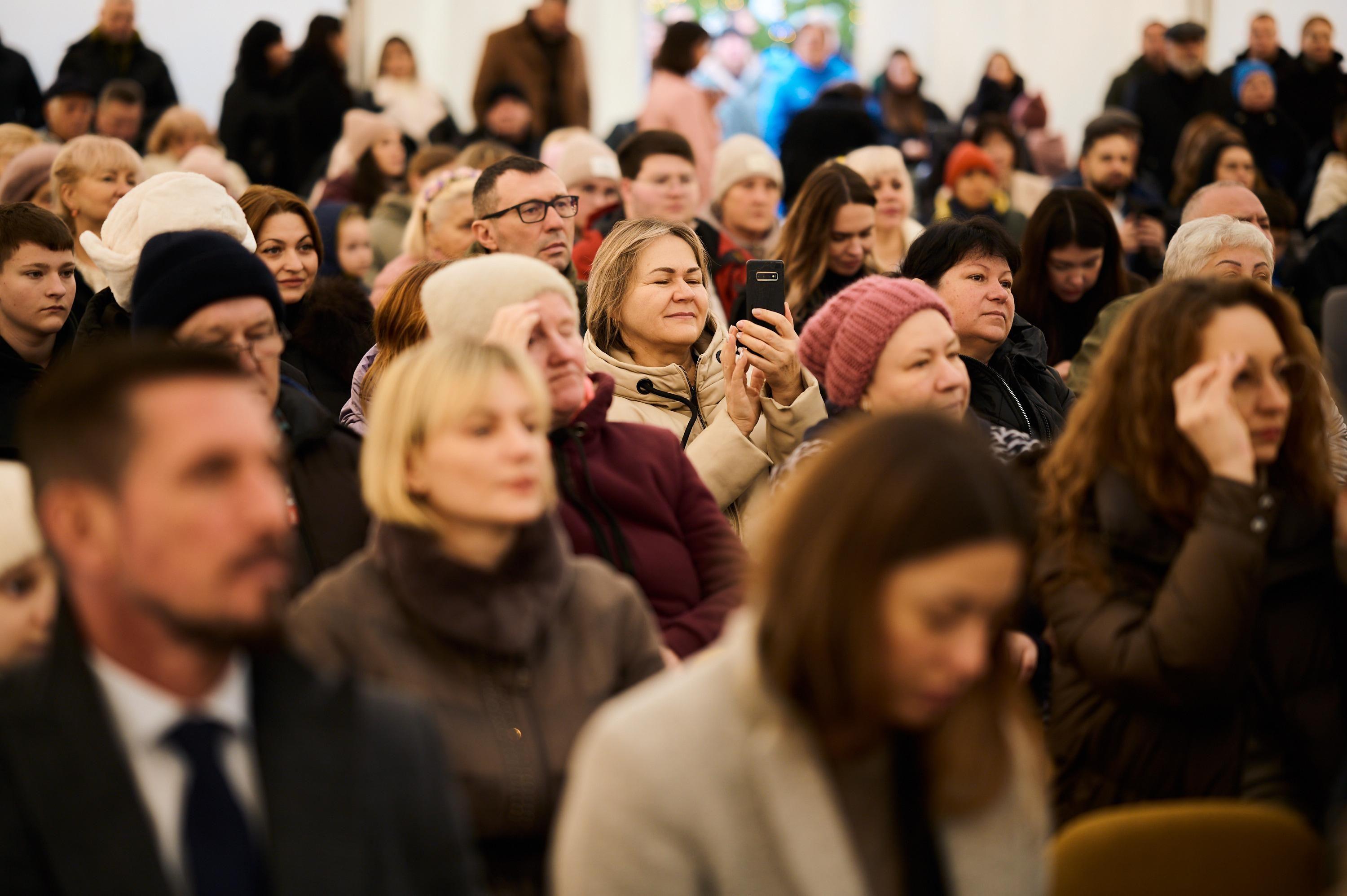 На фото жінки та чоловіки сидять у залі