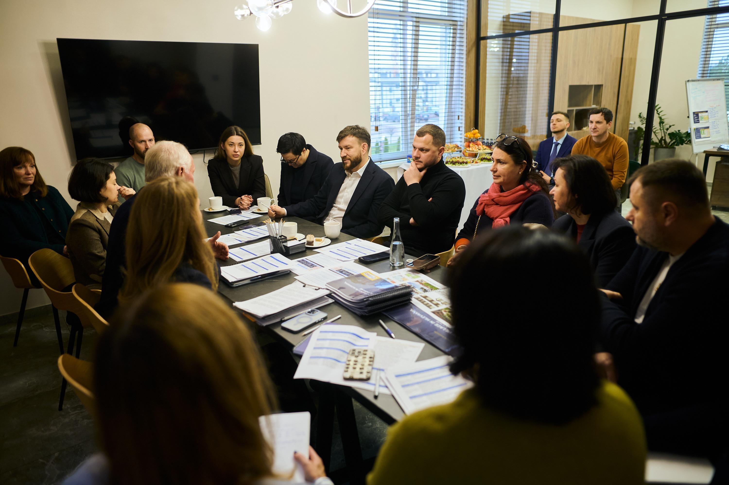 На фото жінки та чоловіки сидять за столом під час зустрічі