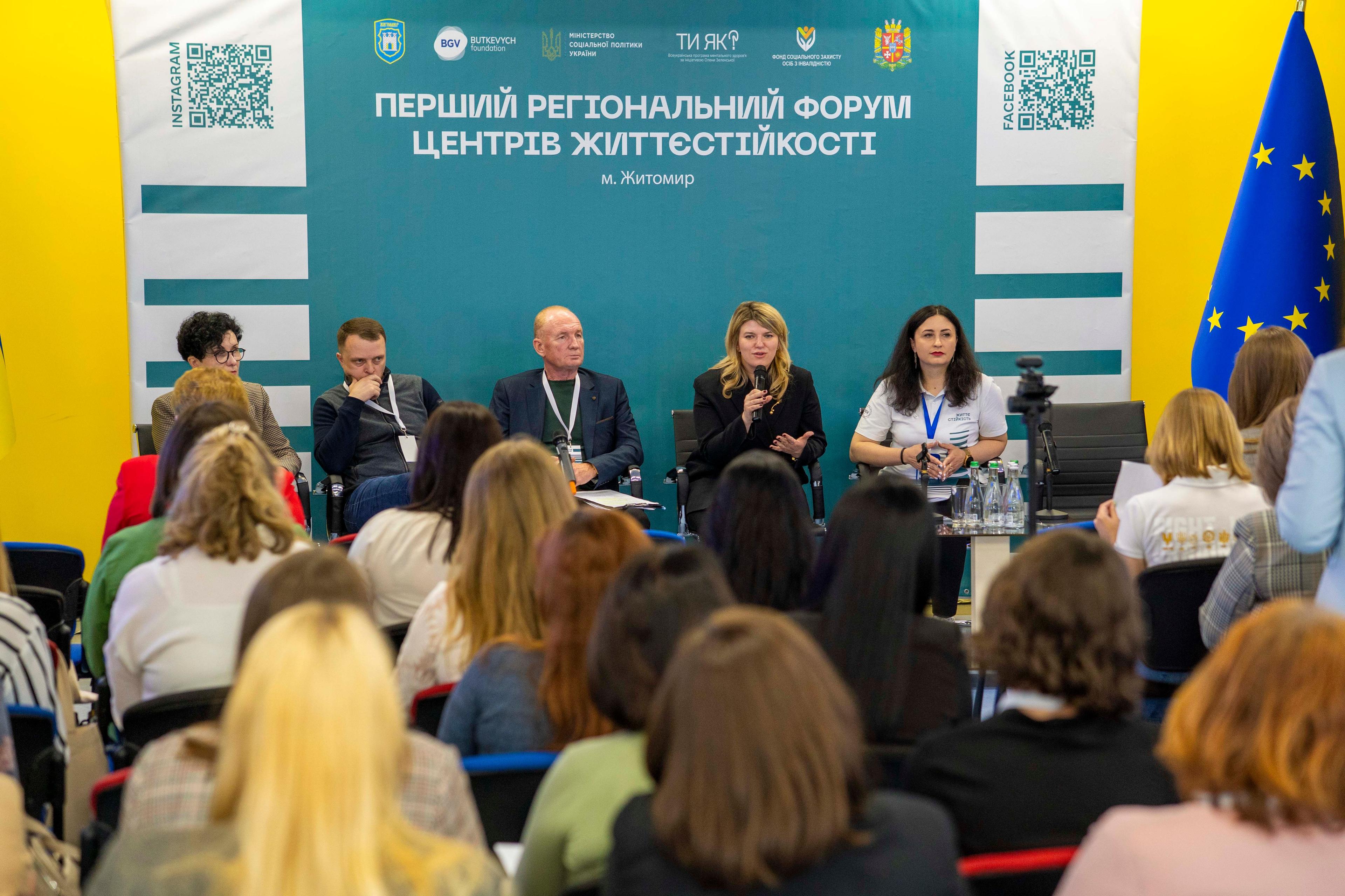 На фото чоловік і жінки сидять на фоні банеру