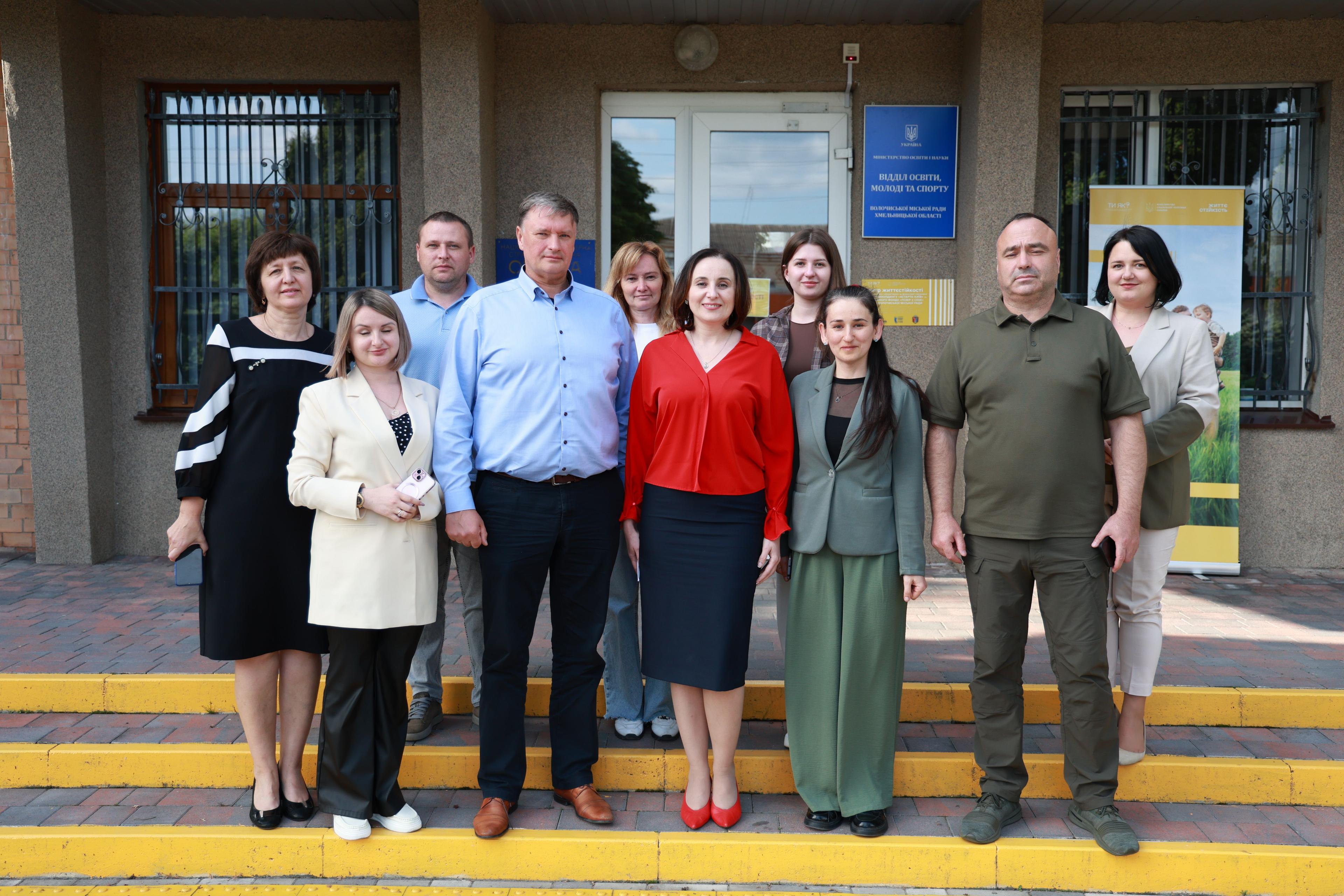 На фото зображено чолвіки і жінки. що стоять на вулиці на фоні приміщення