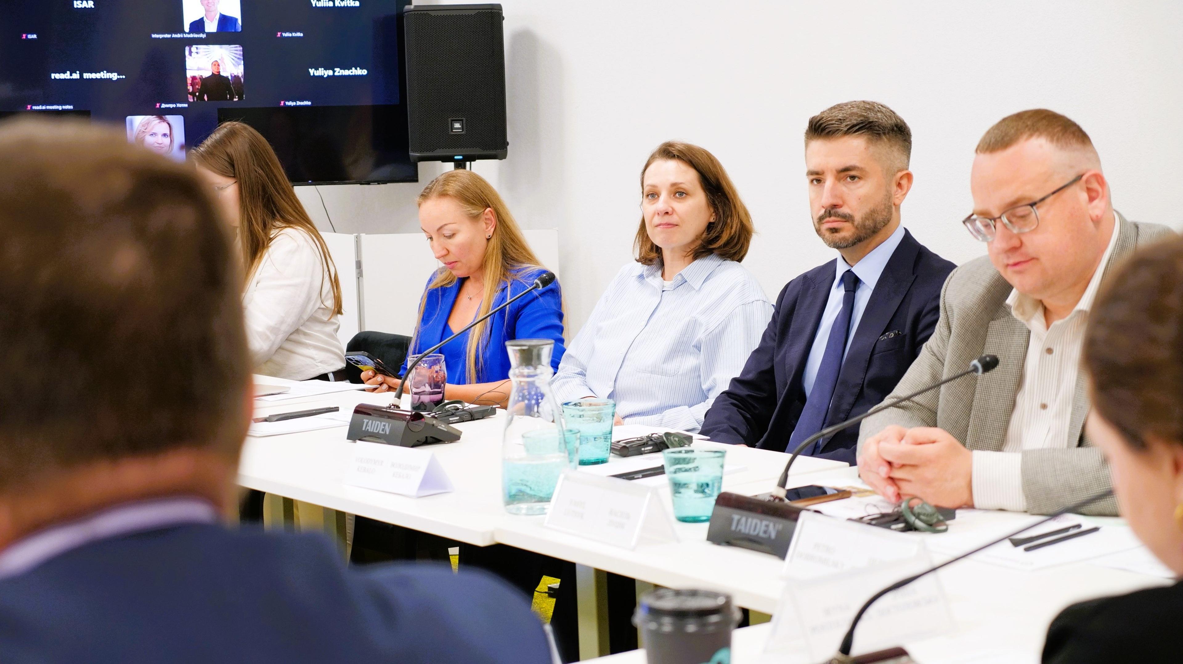 На фото жінки і чоловіки сидять за столом розмовляють
