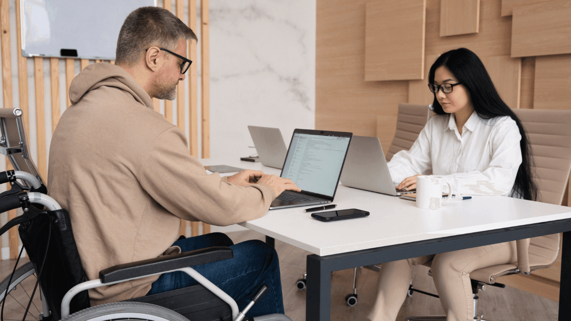 На фото чоловік з інвалідністю та жінка працюють за столом з ноутбками