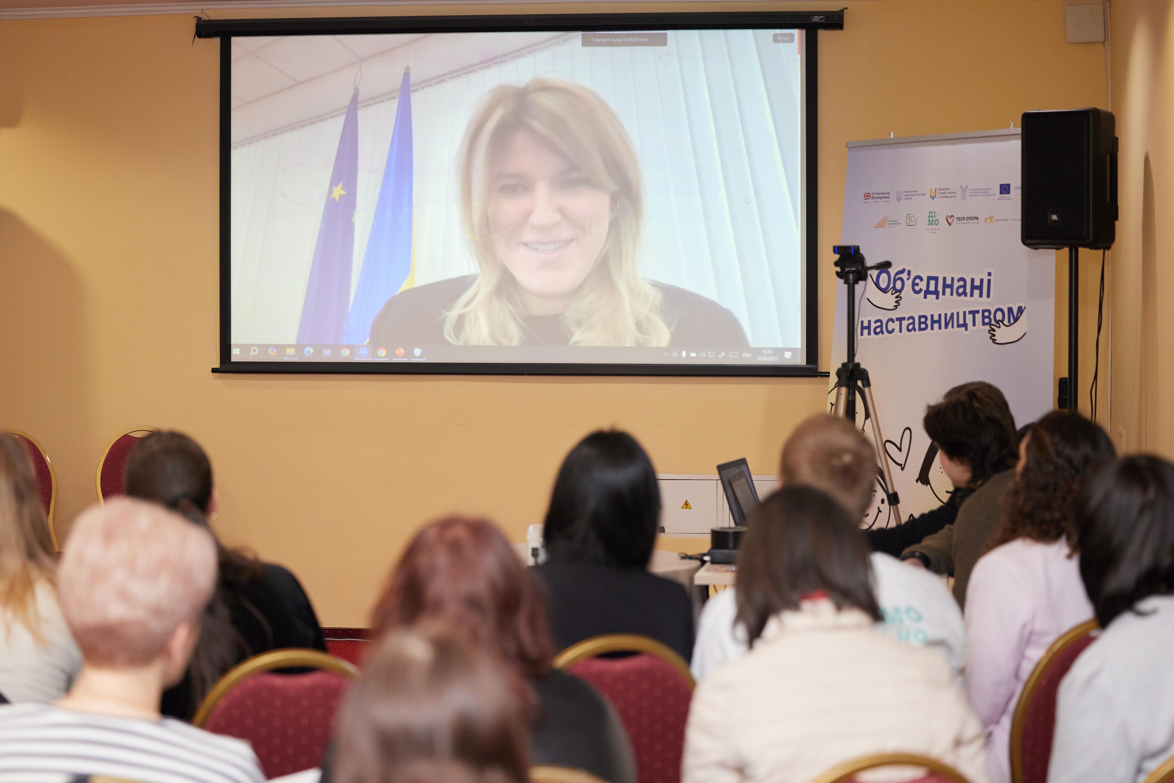 На зображенні люди слухають доповідь у форматі онлайн заступниці Міністерки соціальної політики Ірини Постоловської