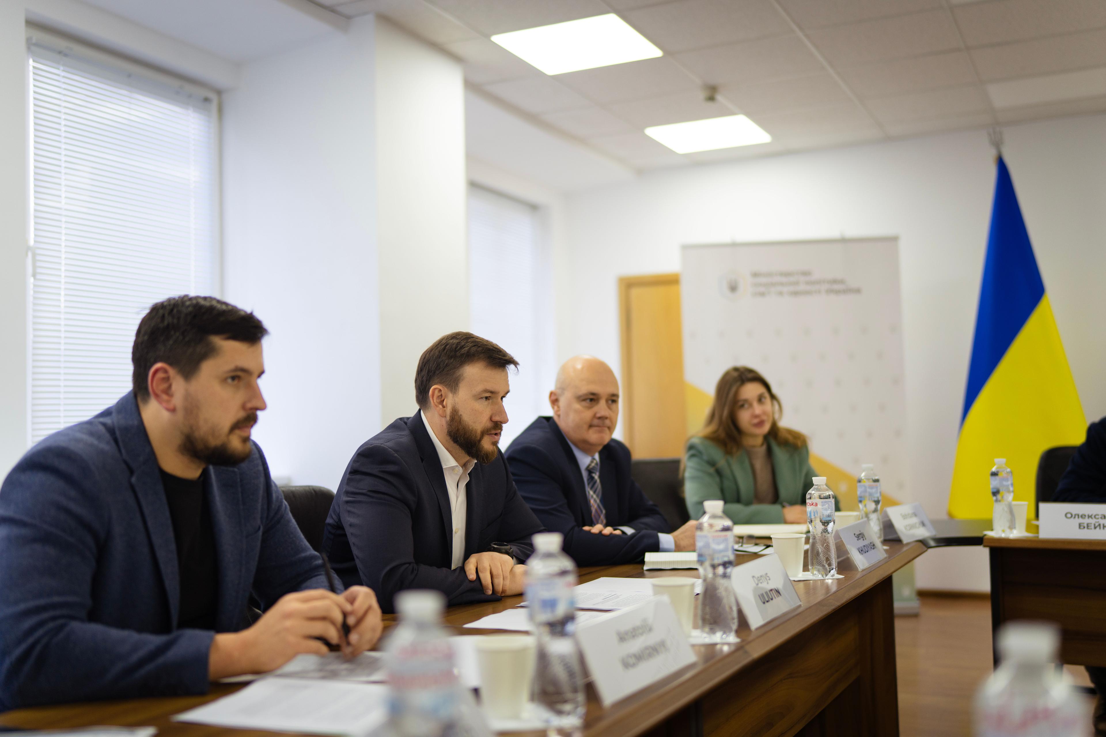 На фото чоловіки та жінка сидять за столом під час зустрічі