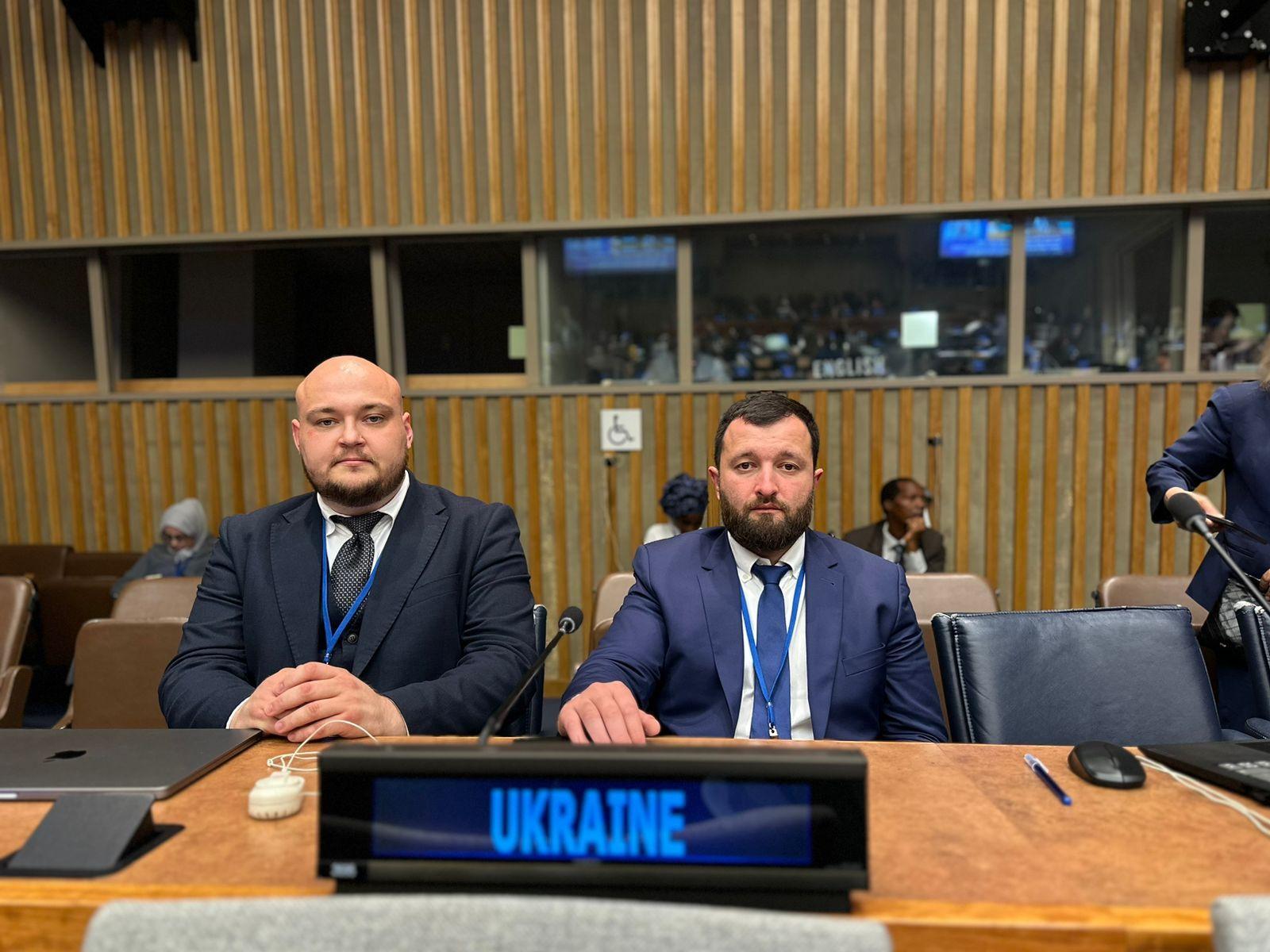 На фото двоє чоловіків сидять в залі на фоні надпису Ukraine