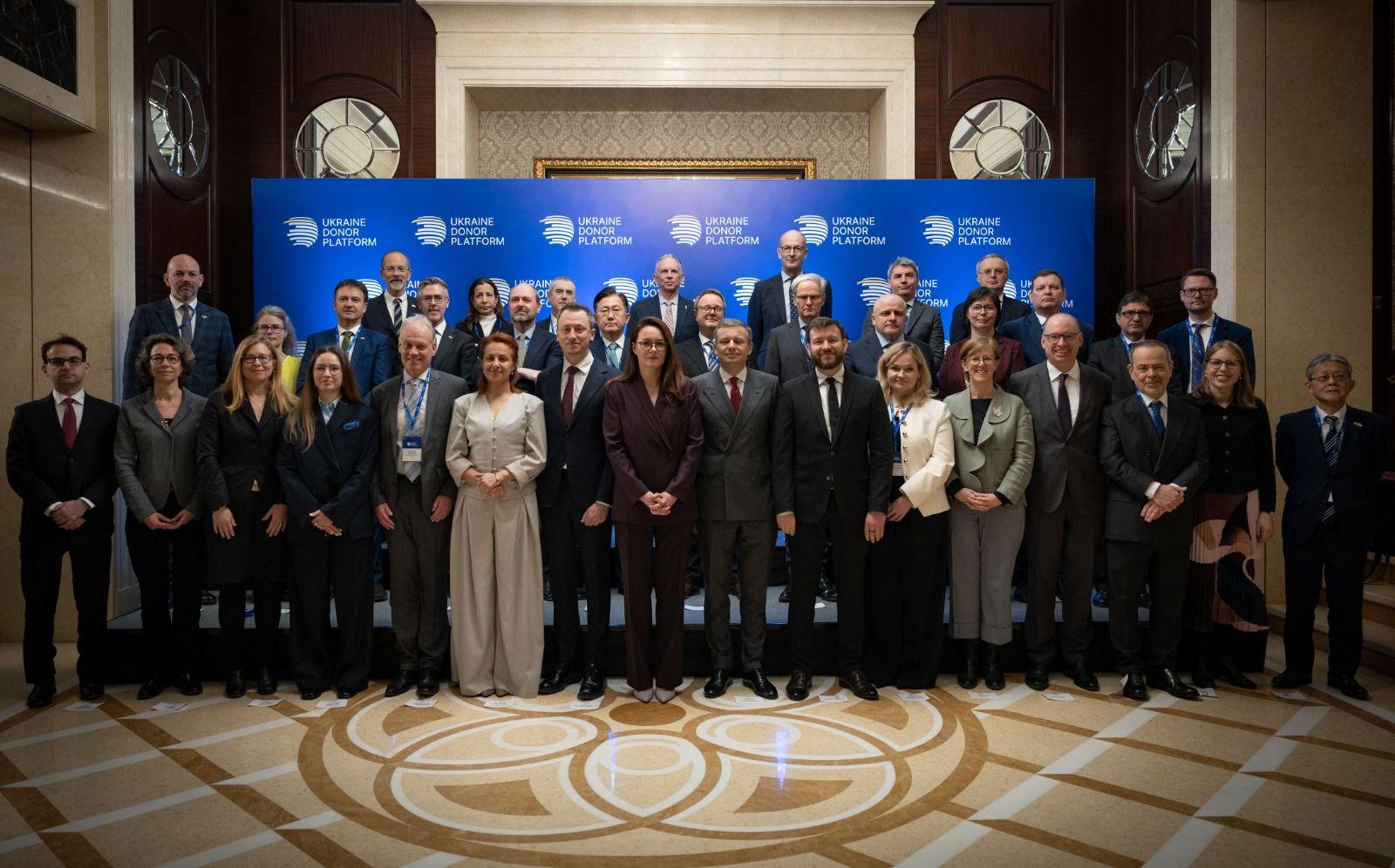 На фото чоловіки та жінки стоять на фоні банеру