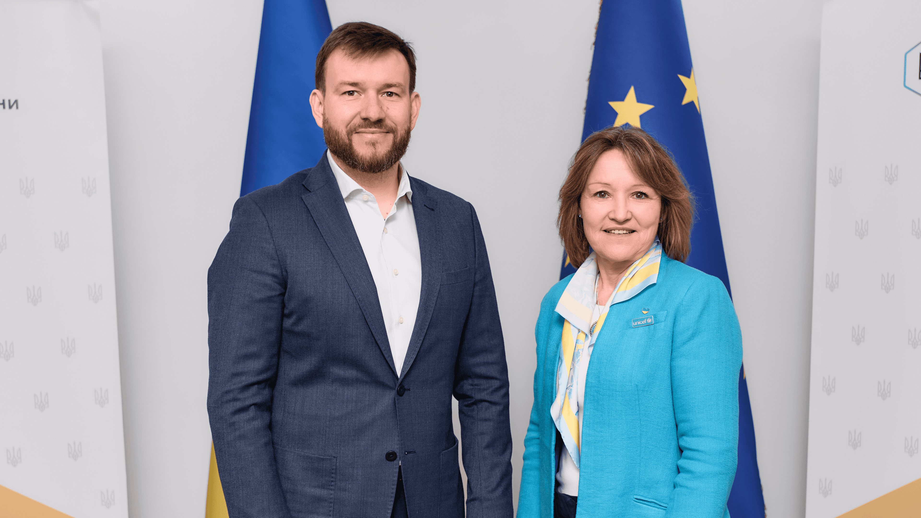 На фото чоловік і жінка стоять на фоні прапорів України та ЄС На фото чоловік і жінка стоять на фоні прапорів України та ЄС