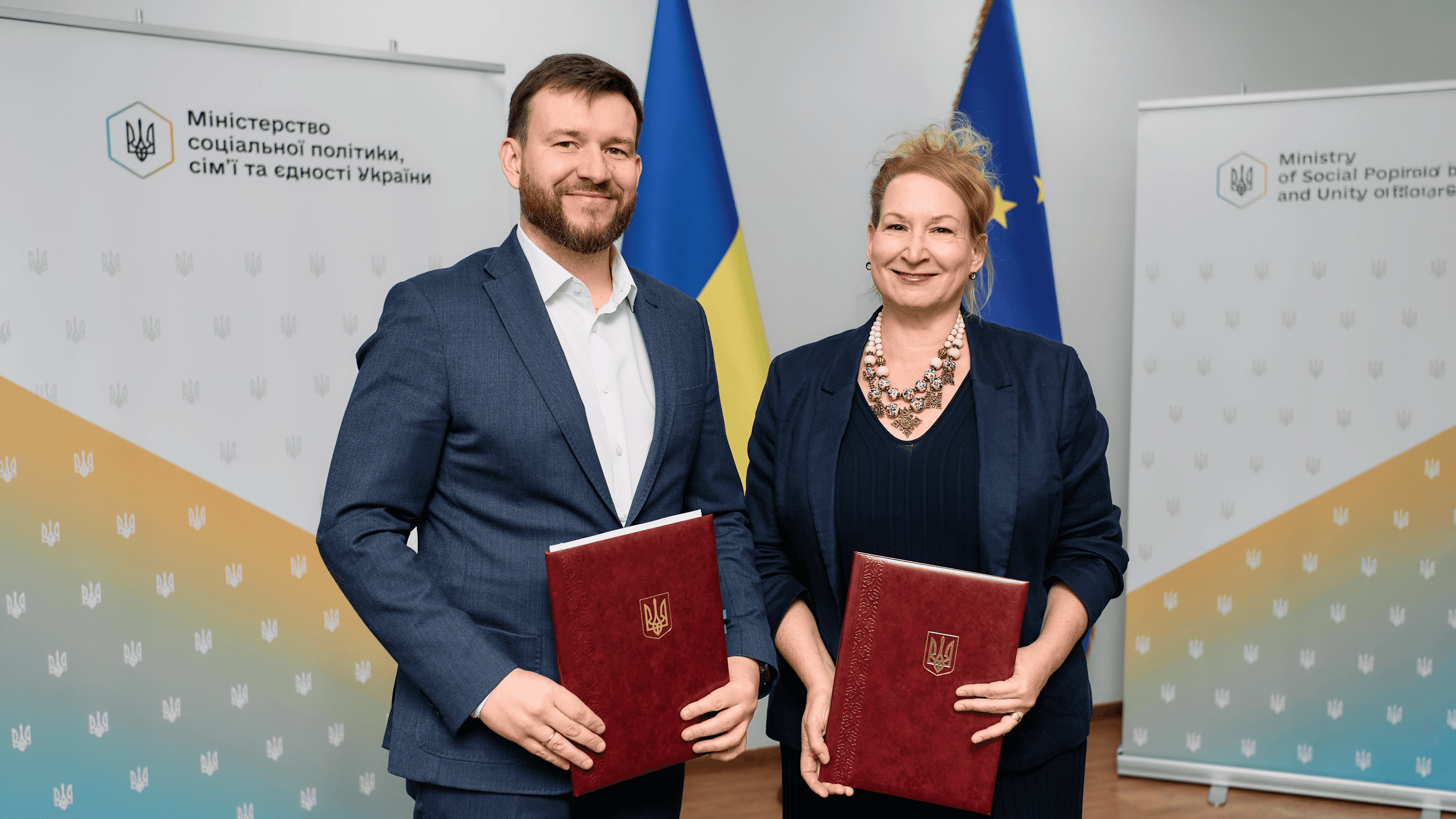 На фото чоловік та жінка тримають в руках документи на фоні прапорів України та ЄС На фото чоловік та жінка тримають в руках документи на фоні прапорів України та ЄС