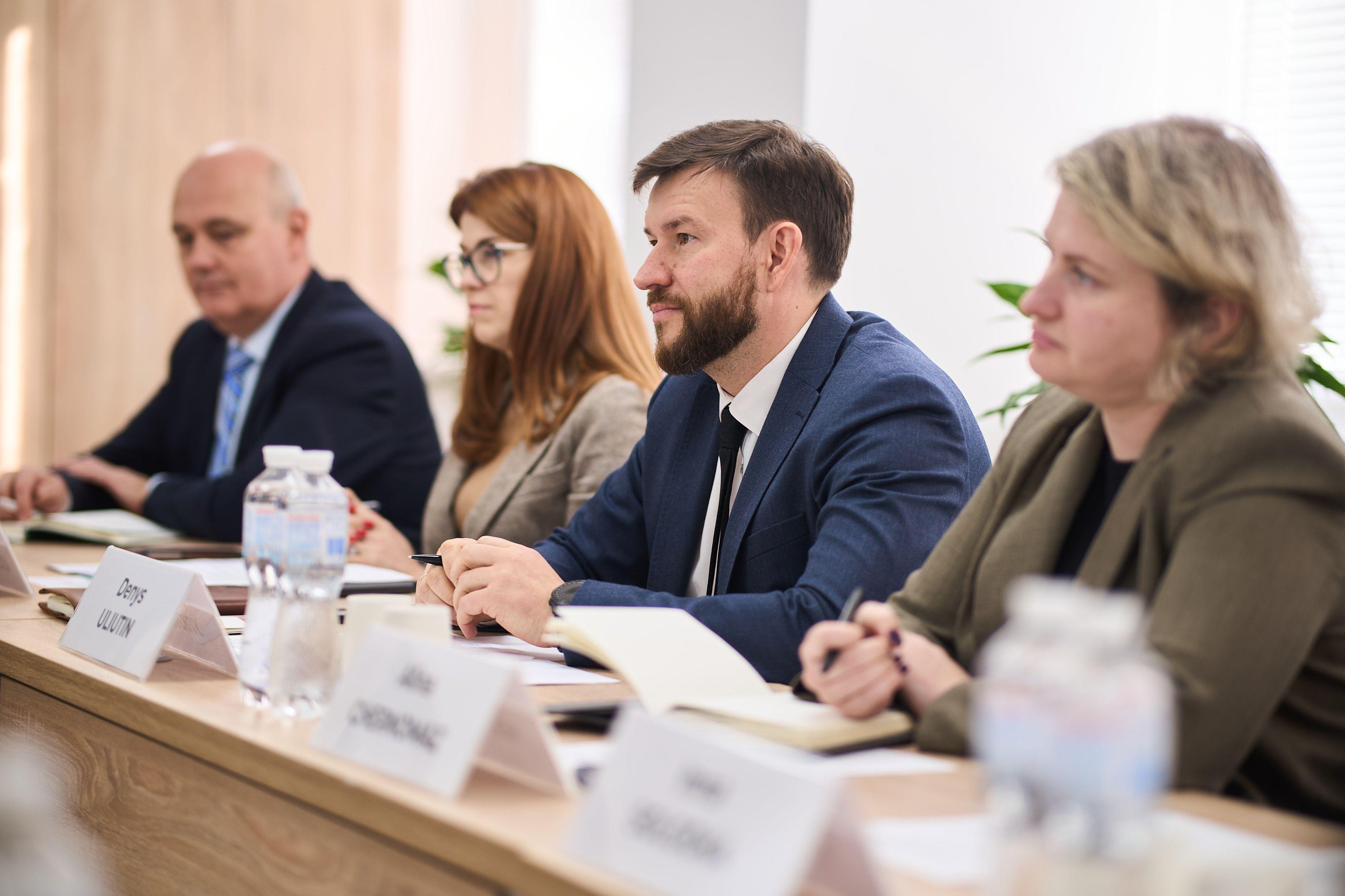 На фото чоловіки та жінки сидять за столом під час зустрічі На фото чоловіки та жінки сидять за столом під час зустрічі