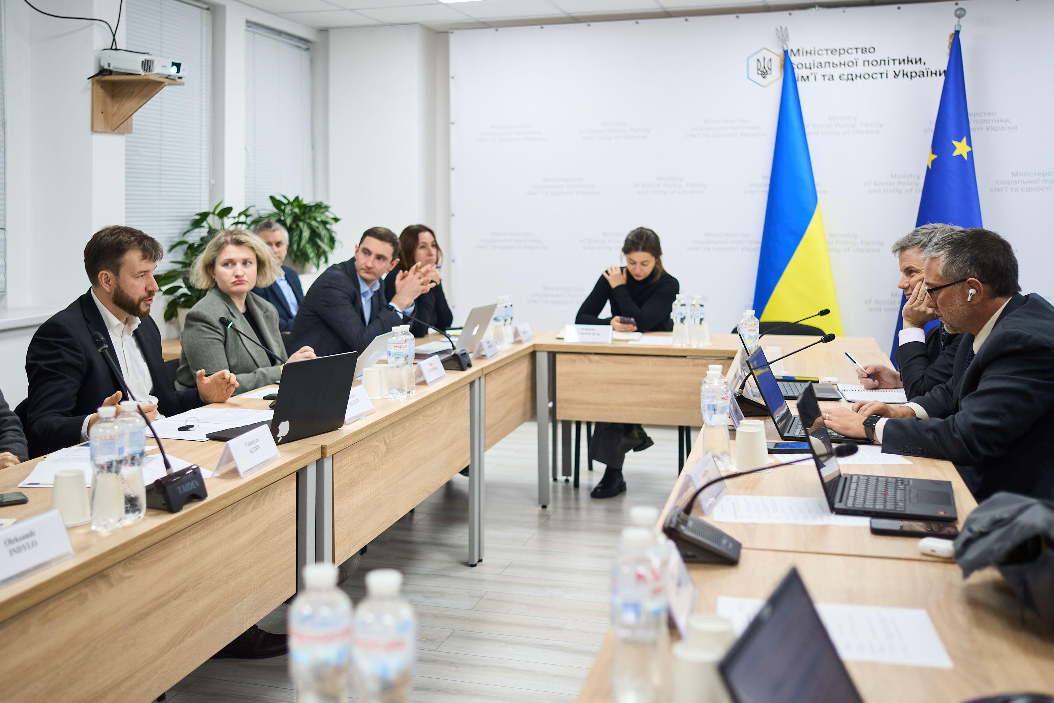 На фото чоловіки та жінки сидять за столом під час зустрічі На фото чоловіки та жінки сидять за столом під час зустрічі