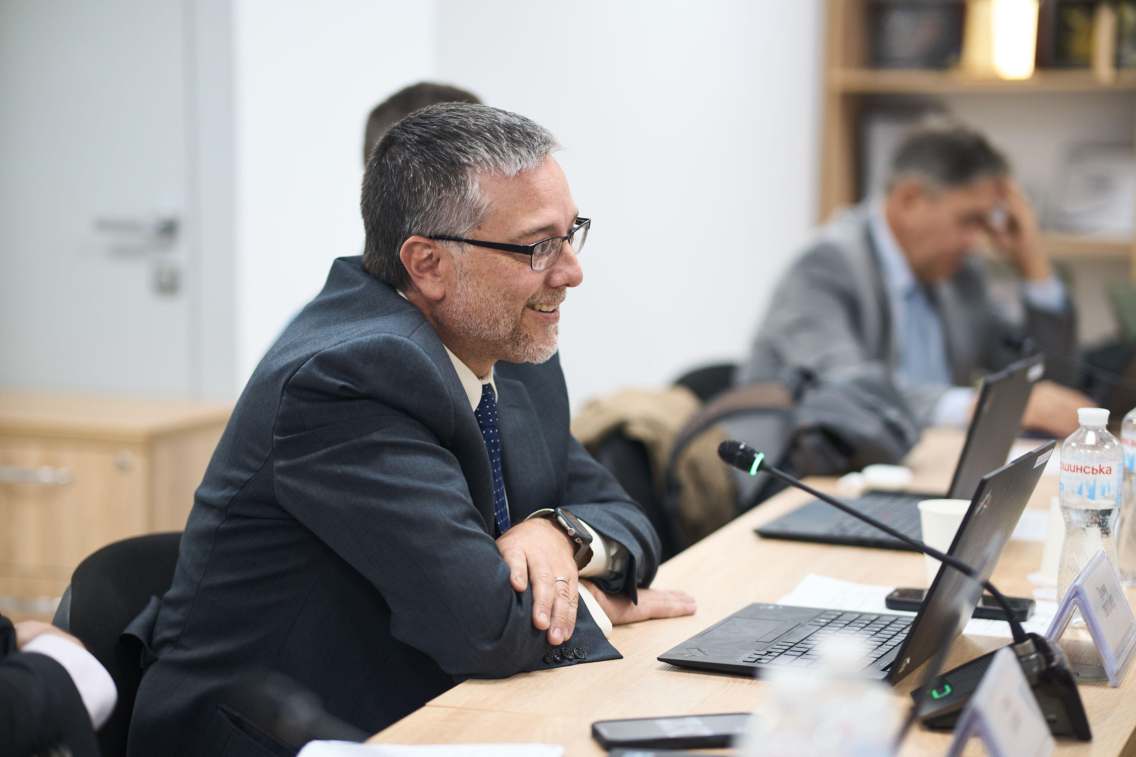 На фото чоловіки сидять за столом під час зустрічі На фото чоловіки сидять за столом під час зустрічі