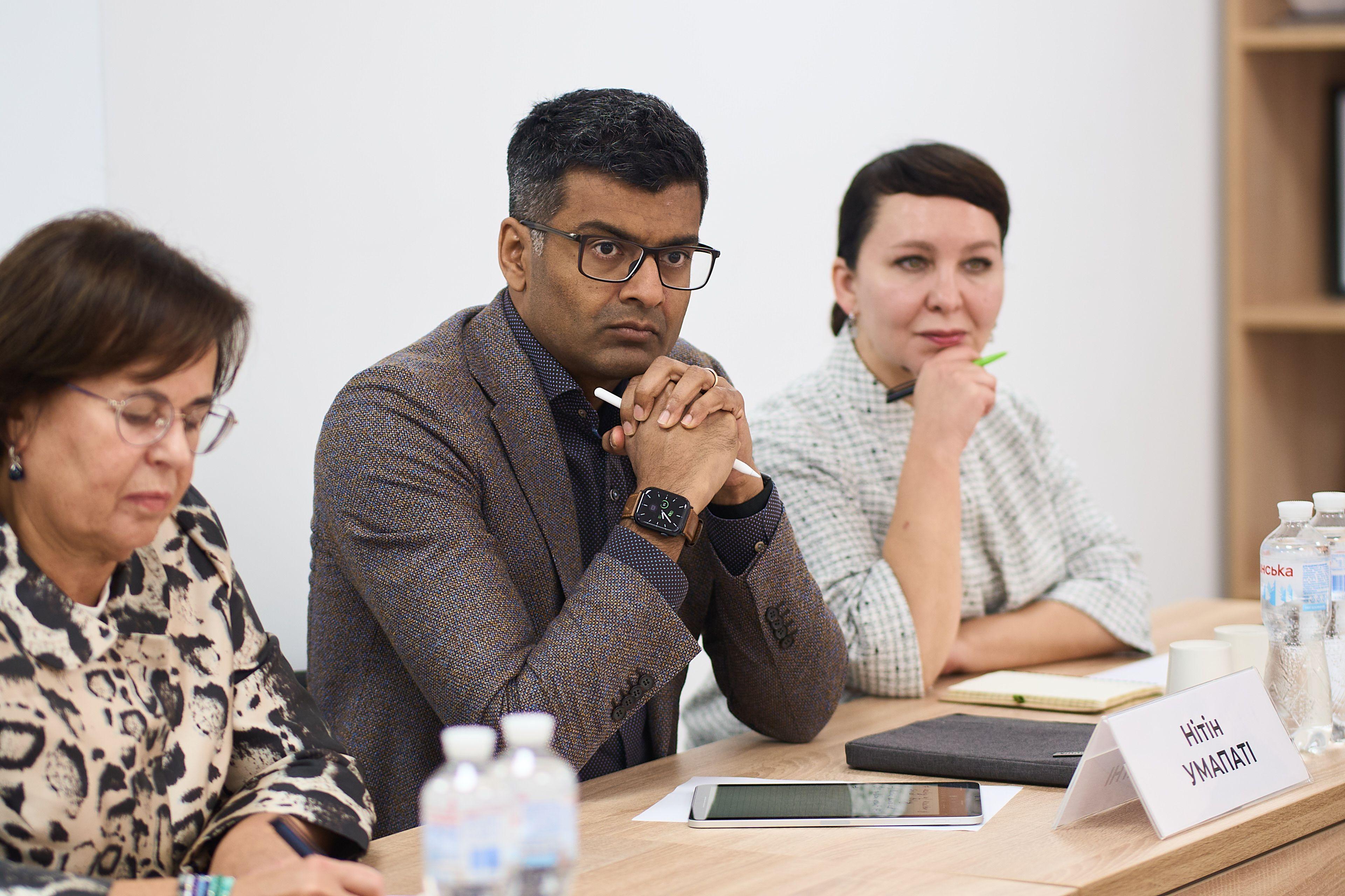 На фото чоловік та жінки сидять за столом під час зустрічі На фото чоловік та жінки сидять за столом під час зустрічі