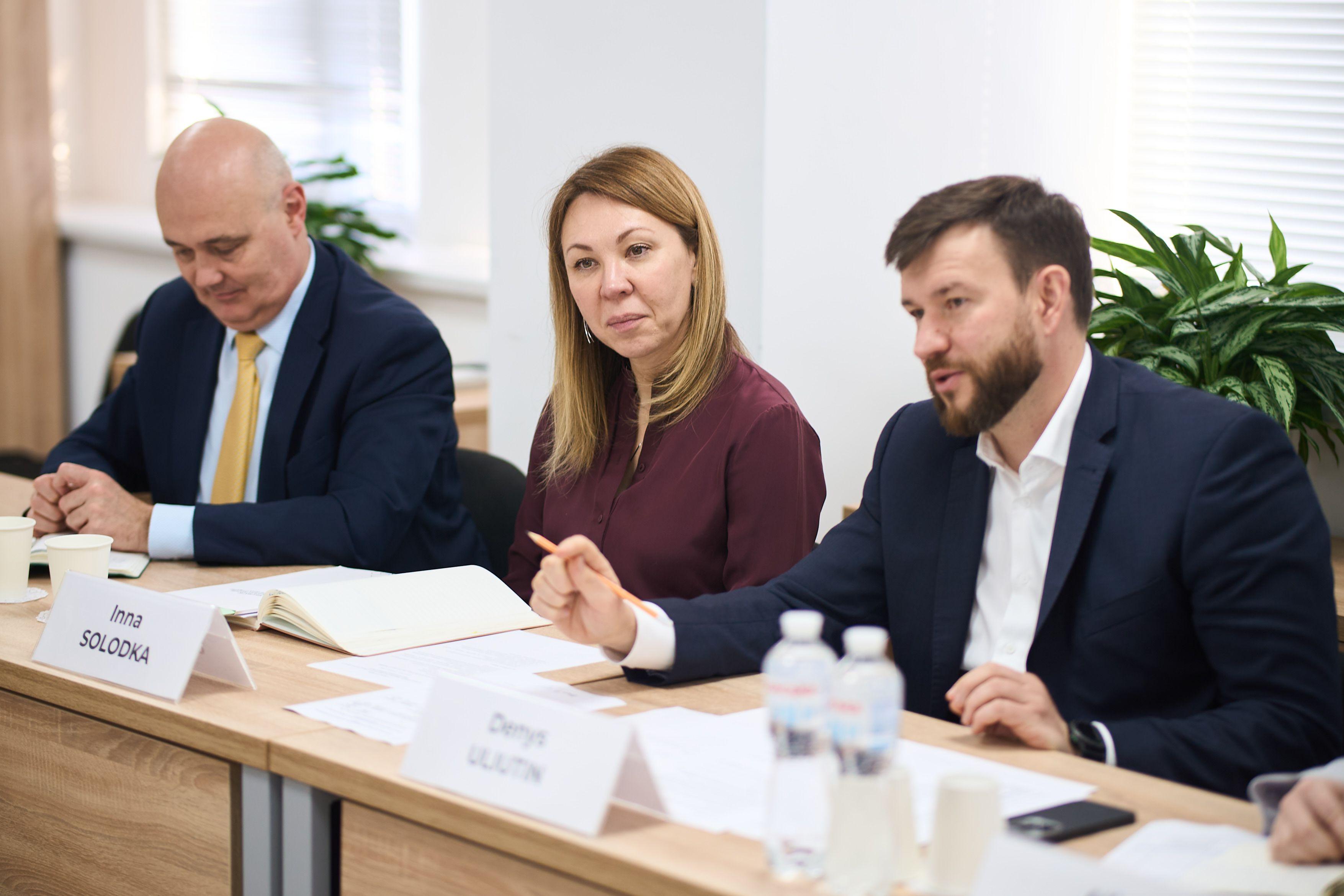 На фото чоловіки та жінка сидять за столом під час зустрічі На фото чоловіки та жінка сидять за столом під час зустрічі