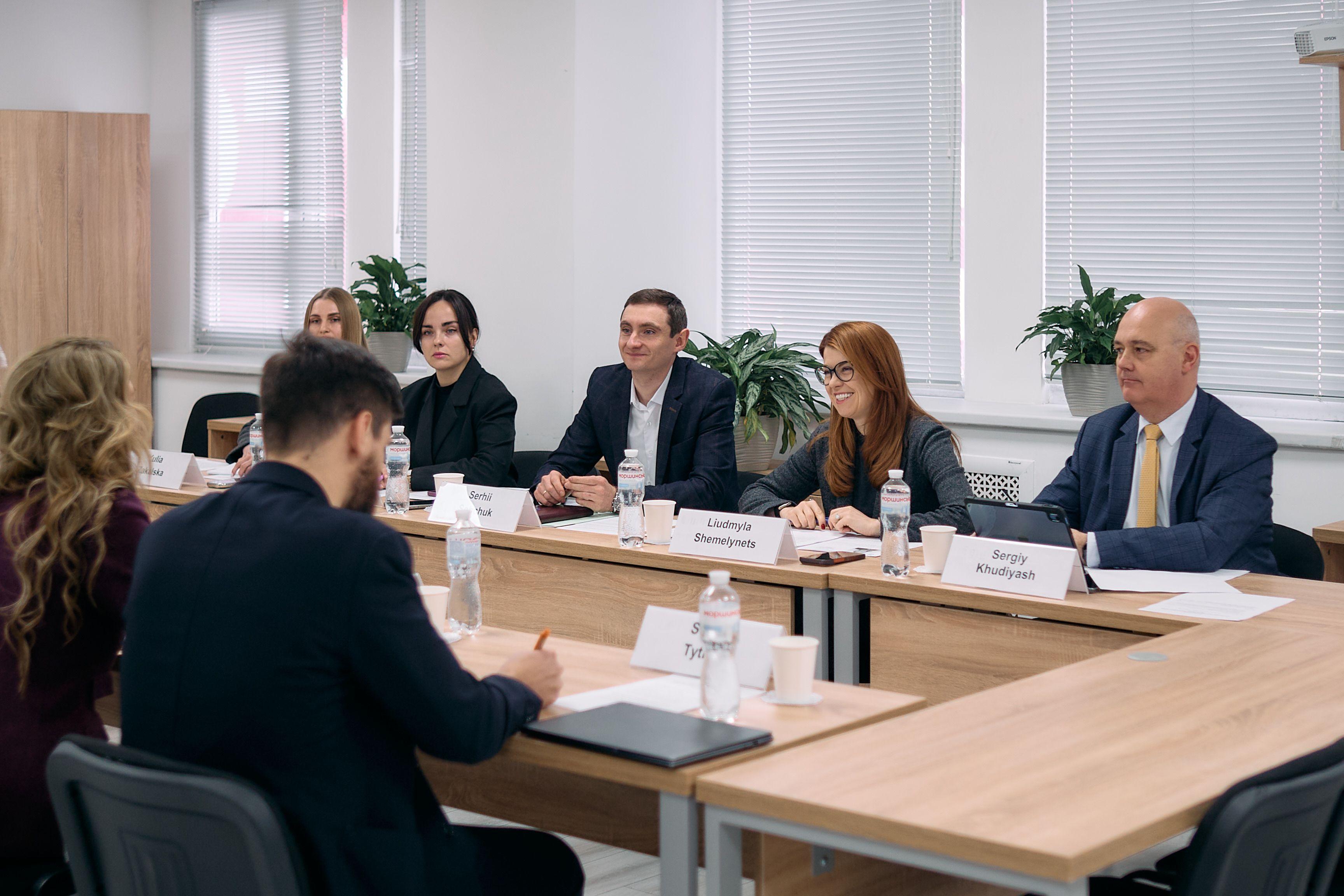 На фото чоловіки та жінки сидять за столом під час зустрічі На фото чоловіки та жінки сидять за столом під час зустрічі