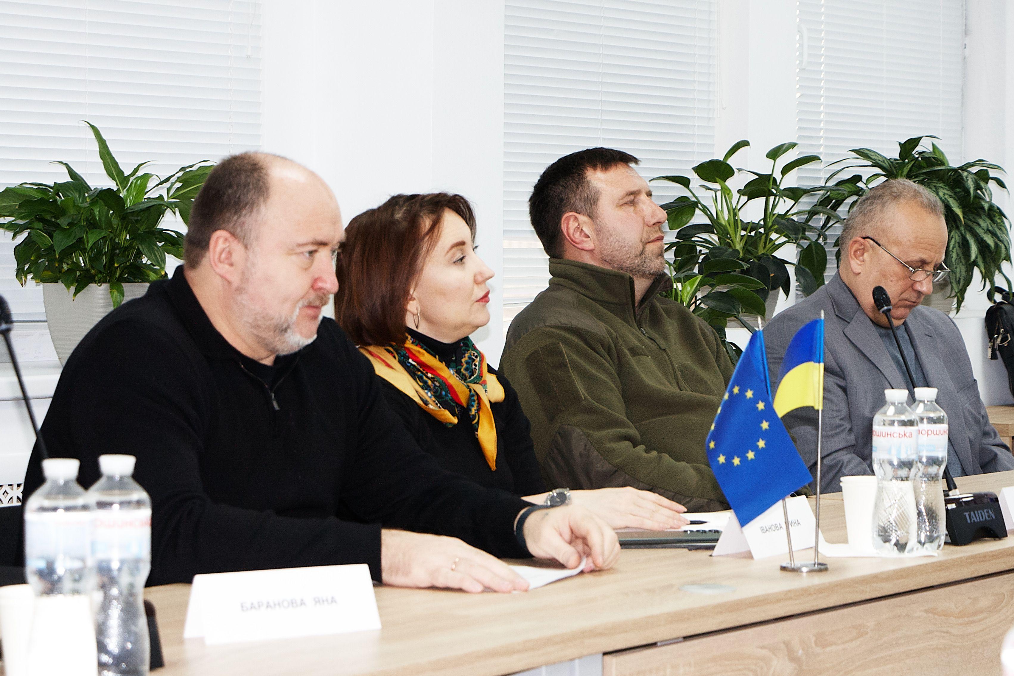 На фото чоловіки та жінки сидять за столом під час засідання Громадської ради На фото чоловіки та жінки сидять за столом під час засідання Громадської ради