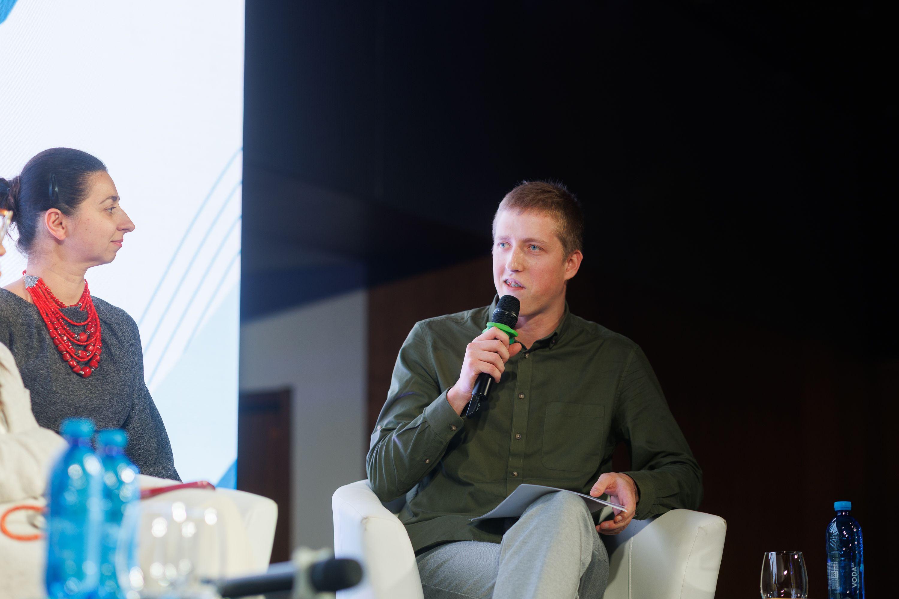 На фото жінка та чоловік сидять на фоні банеру під час заходу На фото жінка та чоловік сидять на фоні банеру під час заходу