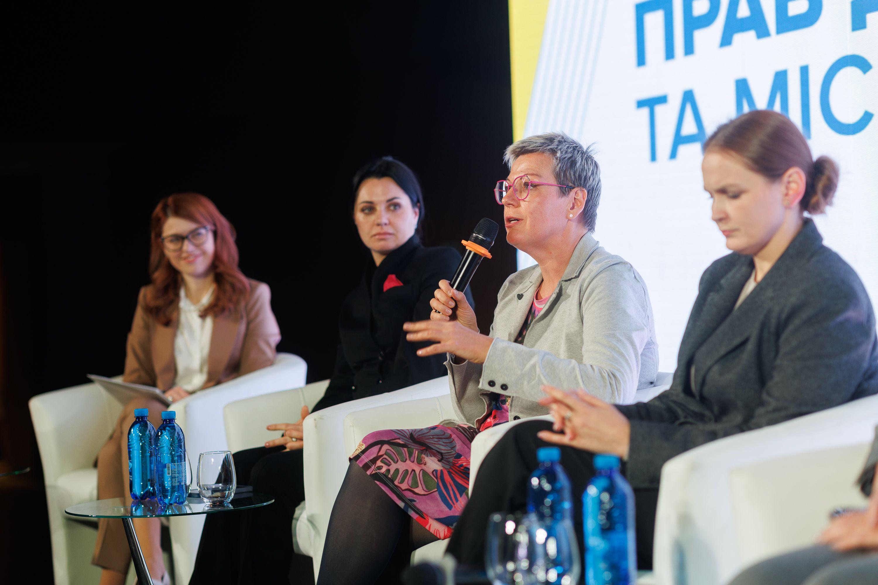 На фото жінки сидять на фоні сцени під час заходу На фото жінки сидять на фоні сцени під час заходу