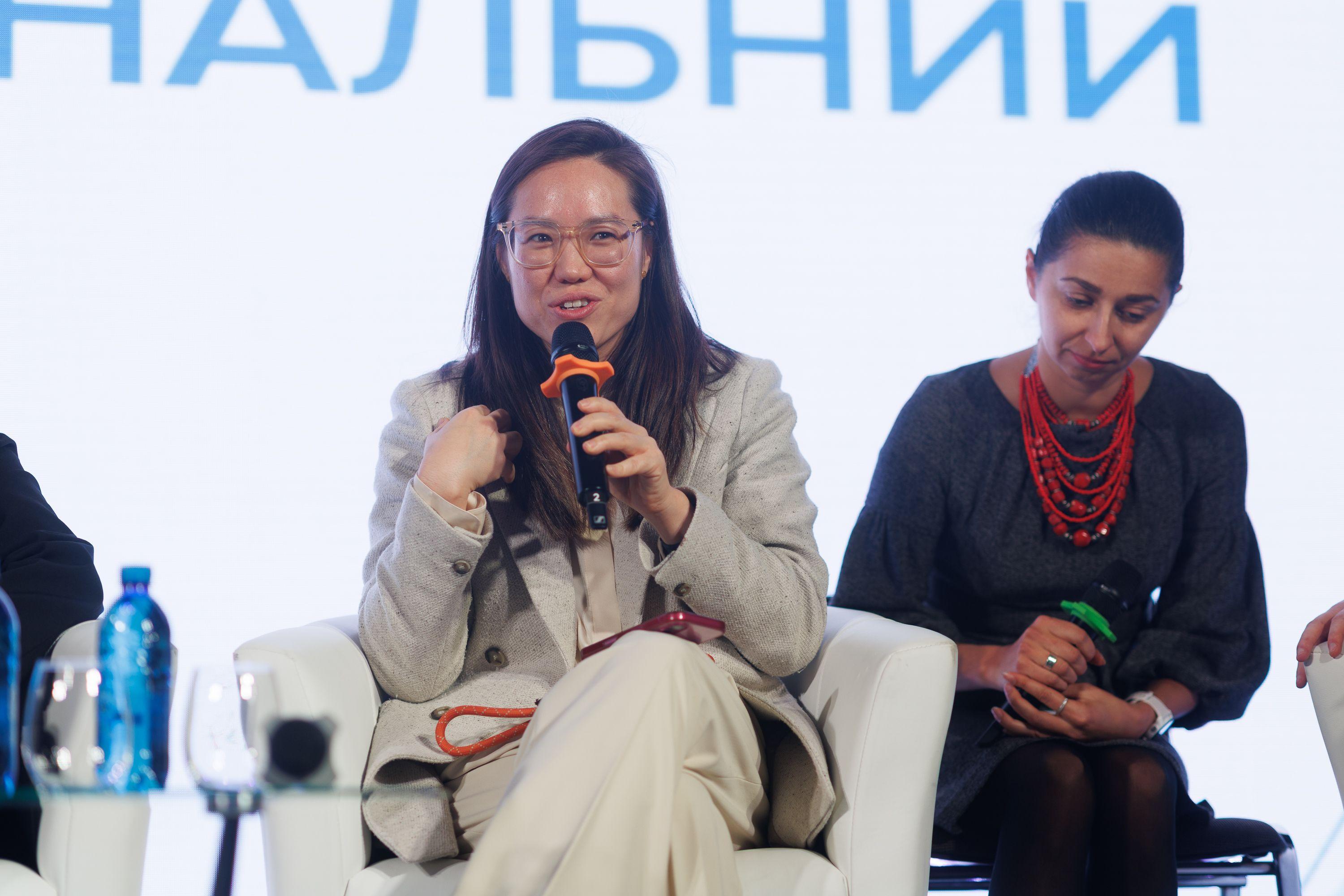 На фото жінка з мікрофоном виступає під час заходу На фото жінка з мікрофоном виступає під час заходу