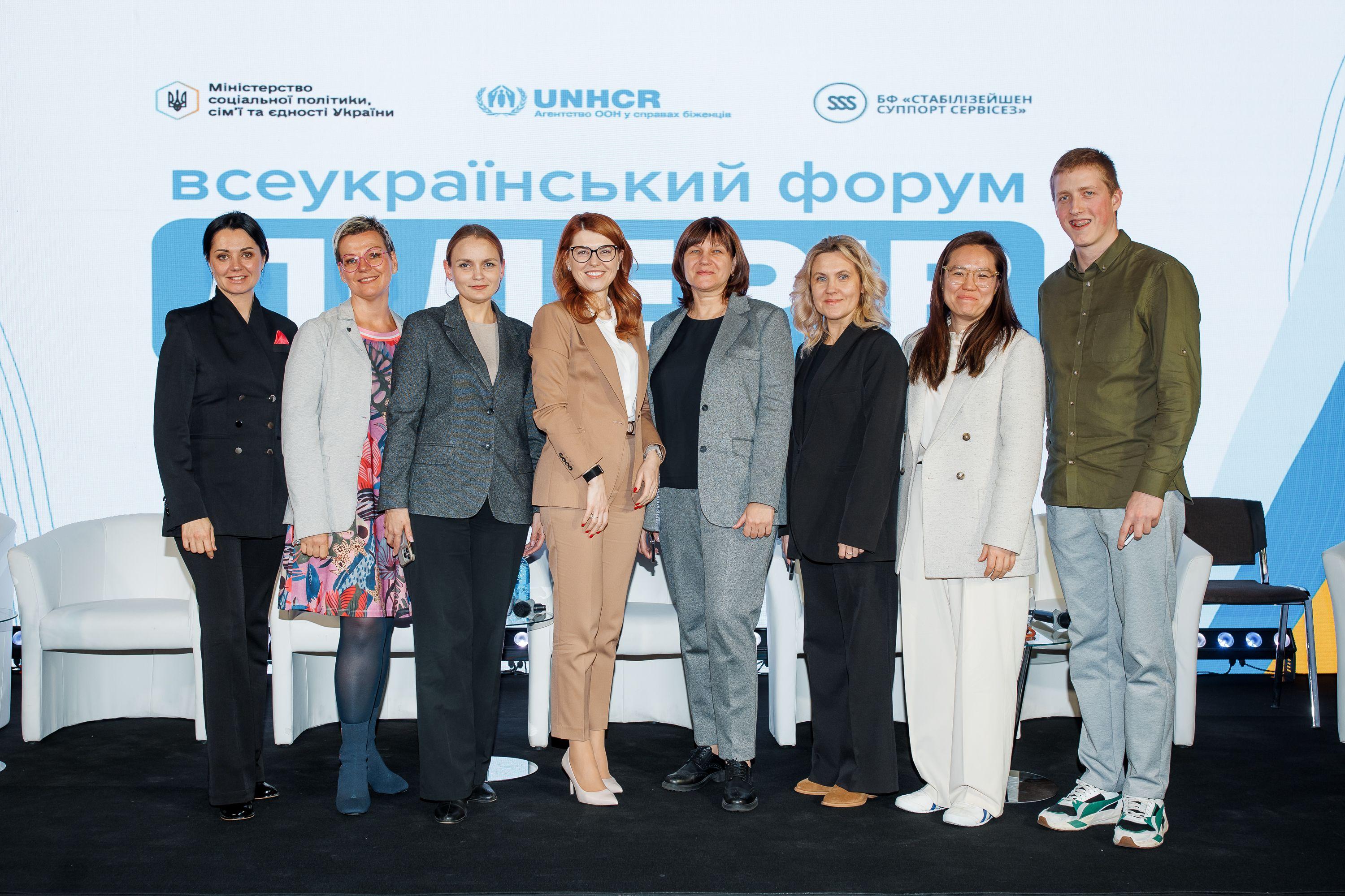 На фото жінки та чоловік стоять на фоні банеру На фото жінки та чоловік стоять на фоні банеру