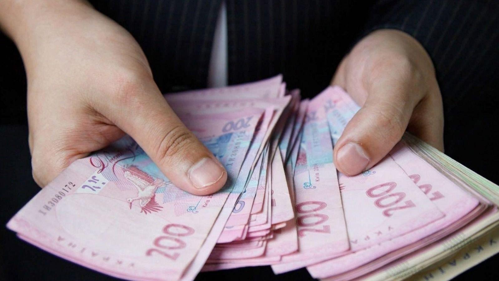 На фото зображено людину, яка тримає в руках грошові купюри На фото зображено людину, яка тримає в руках грошові купюри