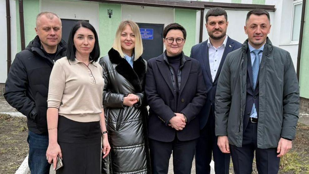 На фото жінки та чоловіки стоять на вулиці на фоні приміщення На фото жінки та чоловіки стоять на вулиці на фоні приміщення